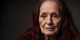Old woman with long red hair looking at the camera with a black background, portrait photography.