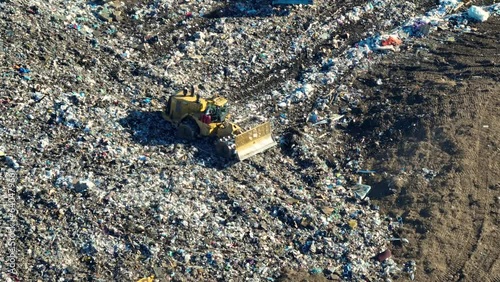 Garbage landfill site with bulldozer tractors burying large amount of trash under the ground. Harmful impact of open waste managment on environment