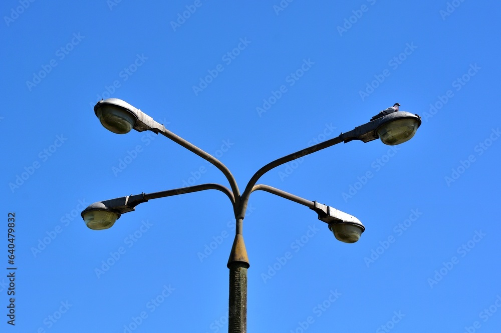 Strong with lots of power old quadruple lantern on a concrete pole top views of lamps against a blue sky without clouds Strong with lots of power old quadruple lantern on a concrete pole top views of lamps against a blue sky without clouds