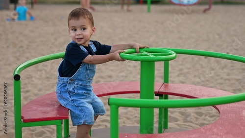 Adorable cute baby sitting on a merry go round. Little Caucasian child spending time on the playground in summer. photo