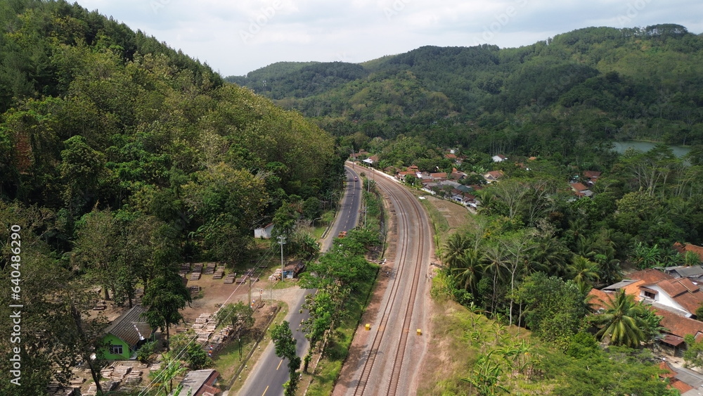 Aerial drone view of highway and railroad tracks among green trees and mountains Aerial drone view of highway and railroad tracks among green trees and mountains