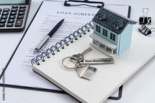 Classic house model, house key with "new homeowner" and calculator on office desk.