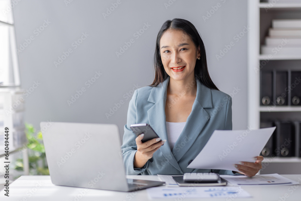 Portrait of young Asian businesswoman in suit, woman smiling and work at workplace inside office, accountant with calculator behind paper phone signing contracts and financial reports Portrait of young Asian businesswoman in suit, woman smiling and work at workplace inside office, accountant with calculator behind paper phone signing contracts and financial reports
