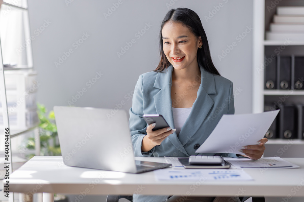 Portrait of young Asian businesswoman in suit, woman smiling and work at workplace inside office, accountant with calculator behind paper phone signing contracts and financial reports Portrait of young Asian businesswoman in suit, woman smiling and work at workplace inside office, accountant with calculator behind paper phone signing contracts and financial reports