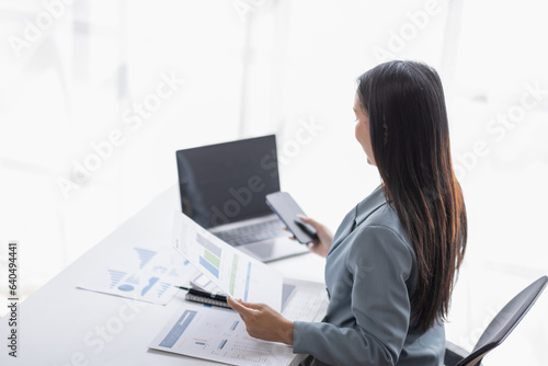 Portrait of young Asian businesswoman in suit, woman smiling and work at workplace inside office, accountant with calculator behind paper phone signing contracts and financial reports