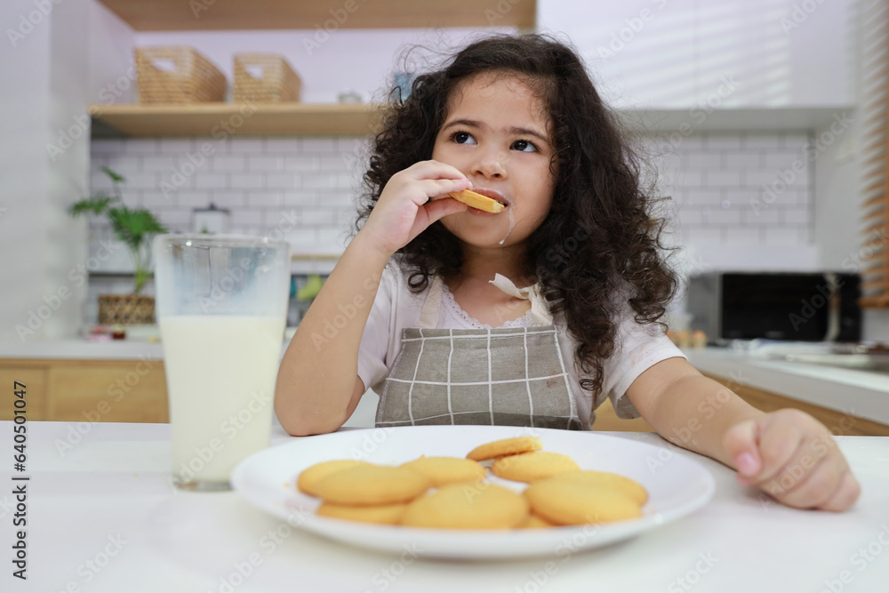 Young hispanic currly hair girl sitting on table and drinking milk while eating vanilla cookies for breakfast with enjoying time. Tasty food and delicious food with happy meal lifestyle kid concept Young hispanic currly hair girl sitting on table and drinking milk while eating vanilla cookies for breakfast with enjoying time. Tasty food and delicious food with happy meal lifestyle kid concept