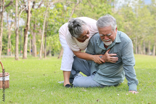 Asian senior man standing and suffering from chest pain or heart attack from walking accident in garden outdoor. Elderly woman caregiver consoling and help him while hugging support. First aid concept © feeling lucky