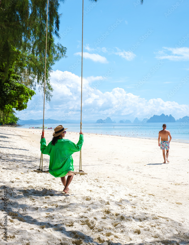 a couple of men and woman on the beach of the tropical Island Naka Island near Phuket Thailand, the woman at a swing on the beach. Naka Island Phuket Thailand