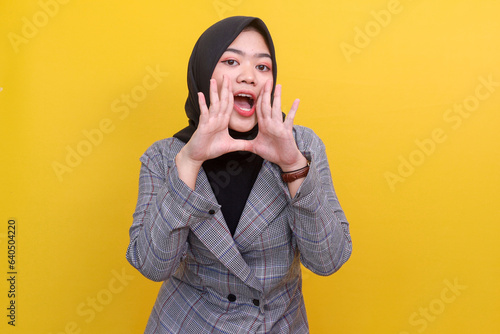Young Asian muslim woman in formal wear gesturing announcement isolated on yellow background photo