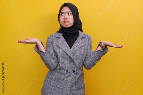 Young Asian muslim woman in formal wear shrugging shoulders with confused expression