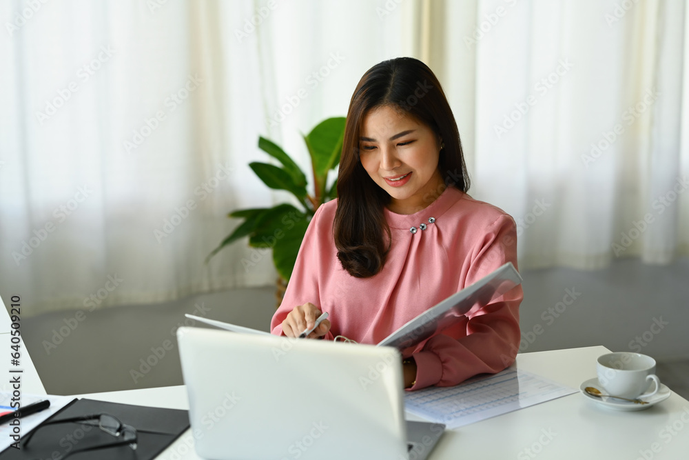Beautiful businesswoman analyzing marketing data, statistics, financial results at desk