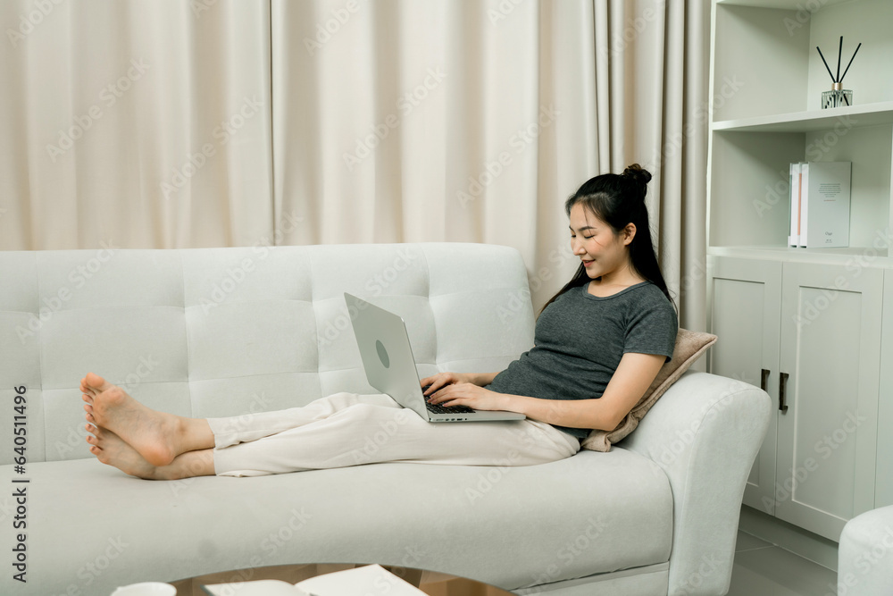 Asian woman sits back on the sofa using a laptop computer to work at home. Asian woman sits back on the sofa using a laptop computer to work at home.