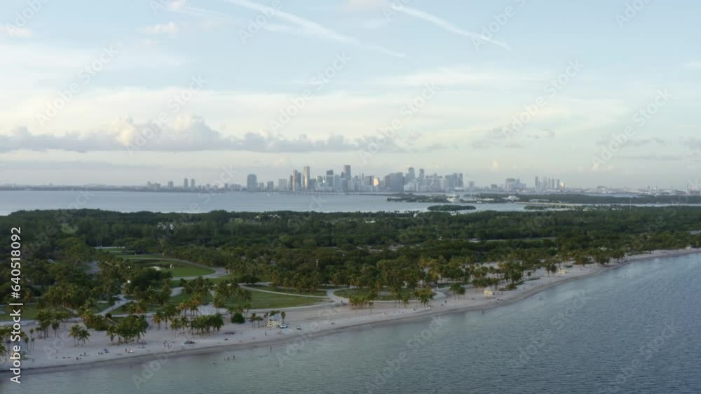 Trucking right aerial drone shot of the beautiful tropical beach surrounded by palm trees on Crandon Park in Key Biscayne with the skyline of Miami, Florida in the distance on a sunny summer evening Trucking right aerial drone shot of the beautiful tropical beach surrounded by palm trees on Crandon Park in Key Biscayne with the skyline of Miami, Florida in the distance on a sunny summer evening