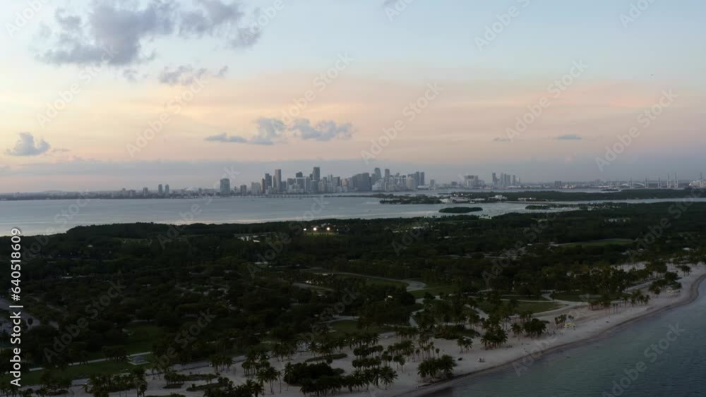 Dolly out descending aerial drone shot of the tropical beach surrounded by palm trees on Crandon Park in Key Biscayne with the skyline of Miami, Florida in the distance on a sunny summer evening Dolly out descending aerial drone shot of the tropical beach surrounded by palm trees on Crandon Park in Key Biscayne with the skyline of Miami, Florida in the distance on a sunny summer evening