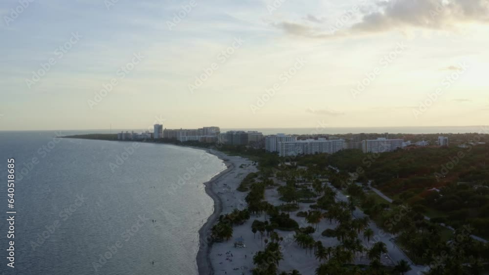 Left trucking aerial drone shot of the beautiful tropical beach coastline surrounded by palm trees and resorts on Crandon Park in Key Biscayne outside of Miami, Florida on a warm sunny summer evening Left trucking aerial drone shot of the beautiful tropical beach coastline surrounded by palm trees and resorts on Crandon Park in Key Biscayne outside of Miami, Florida on a warm sunny summer evening