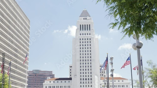 View onto the city hall of Los Angeles near while airplane passing near Clara Shortridge Folz Criminal Justice center of the Gloria Monila Grand Park during summer time american flags in front steady photo