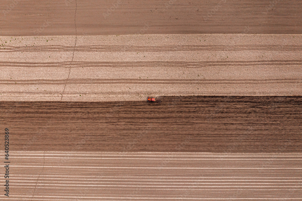 Fototapeta premium Agricultural tractor with tiller attached performing field tillage before the sowing season, aerial shot seen from the drone pov
