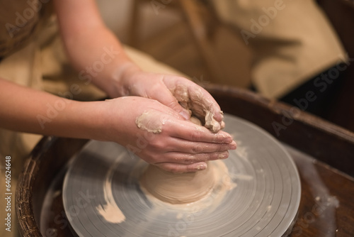 Potter girl works on potter's wheel, making ceramic pot out of clay in pottery workshop