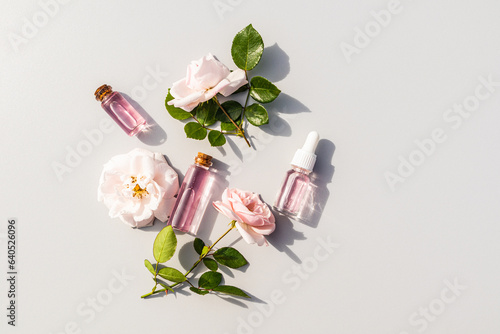 Several different glass cosmetic bottles with serum with bud flower rose extract and rose water for facial skin care. The top view is flat styling