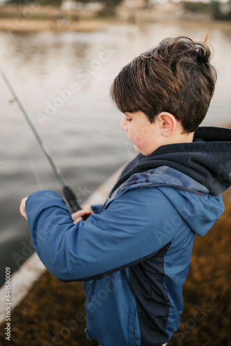 Boy with brown hair fishing in pond with blue jacket on 
