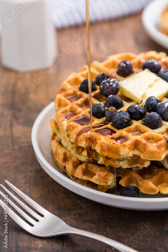 Syrup dripping on Belgian waffle with blueberries for breakfast