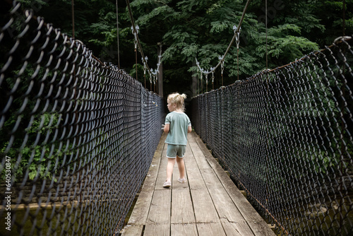 Child walking across swinging bridge in forest