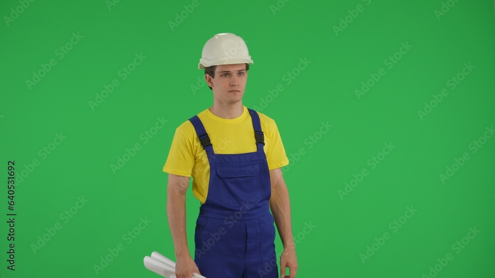 Medium green screen isolated chroma key shot of a young construction worker holding two rolled up plans and looking away.