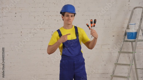 Medium video of a young construction worker standing in the room under renovation, pointing at screwdrivers, turn-screws, recommending the product.