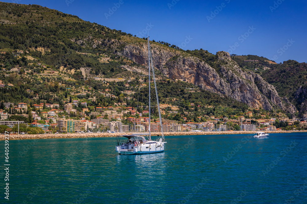 Mediterranean Sea and coastline with a beach and a boat in the water in Menton on the French Riviera, South of France on a sunny day