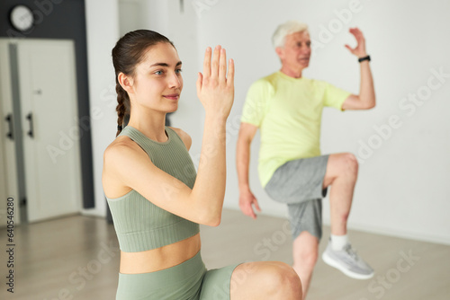 Young fitness instructor exercising with elderly people in studio