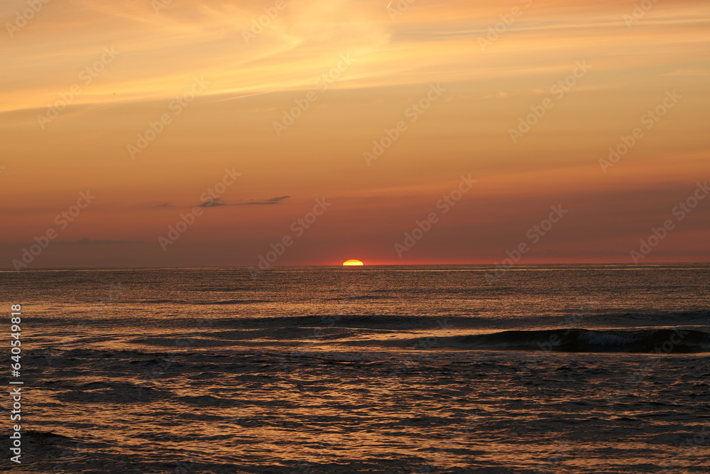 The glowing sun sinking on the horizon of the sea or ocean
