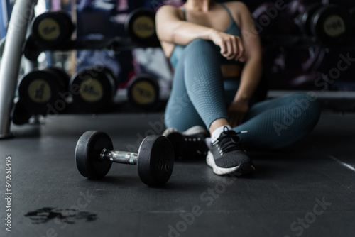 woman doing stretching exercises on the floor and dumbbell in the foreground