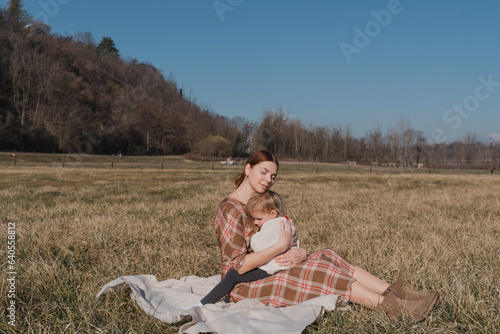 Redhead woman and her baby daughter hugging while sitting in the fieid photo