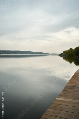 Vertical shot of a landscape with a quiet lake and a wooden pier in the foreground