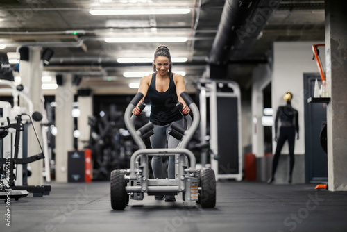 Front view of a happy strong woman pushing weights in a gym during her strength training.