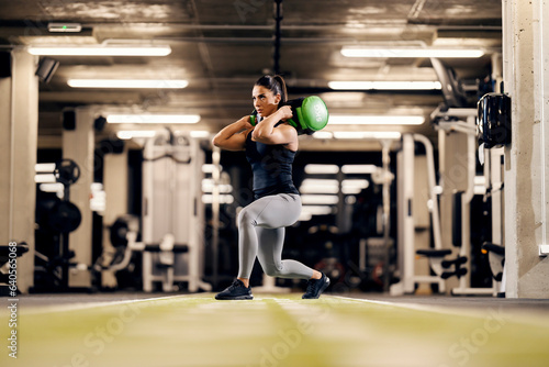 Schilderij op canvas A female bodybuilder is doing lunges with heavy weights on her shoulders in a gym