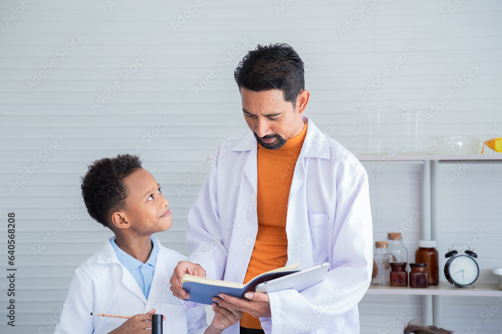 Adorable African American boy school student wearing lab coats happy studying with Indian teacher sending experiment paperwork in laboratory room, lifestyle learning education science class for kid Adorable African American boy school student wearing lab coats happy studying with Indian teacher sending experiment paperwork in laboratory room, lifestyle learning education science class for kid