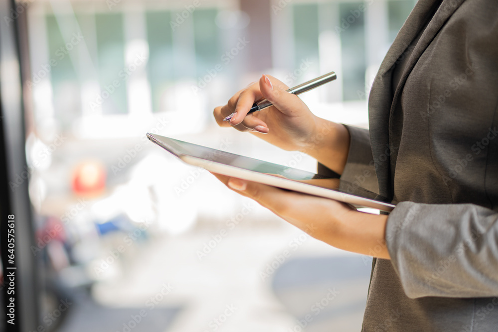 Naklejka premium Smart technology can help you. Businesswoman using digital tablet in office while standing in front of window close up pictures using digital tablet