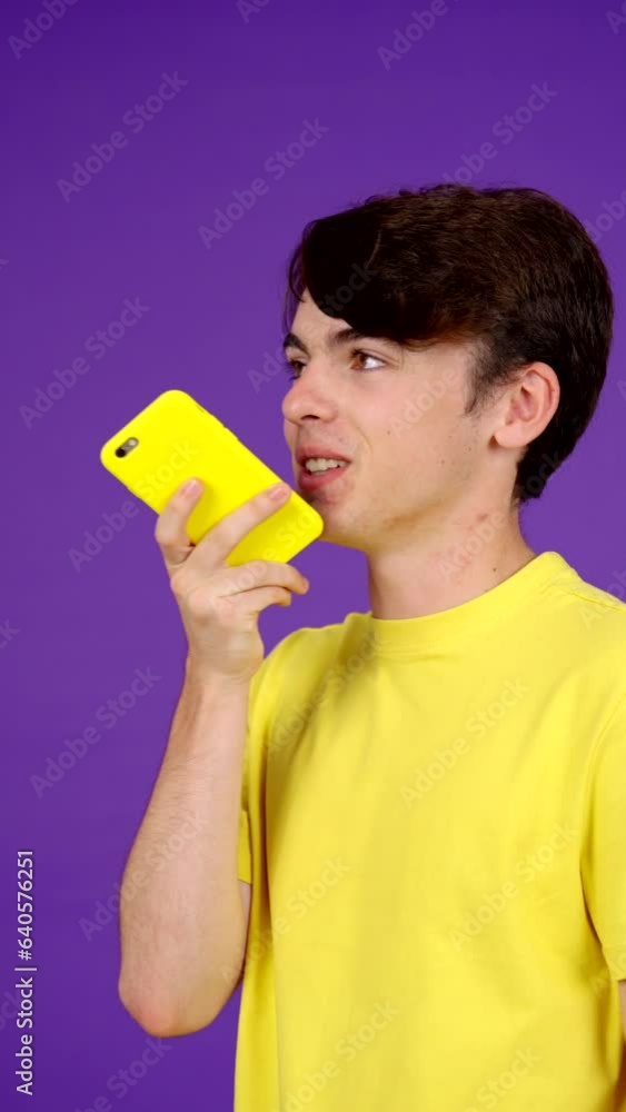 Teenager boy sending voice message or voicemail on phone isolated on purple background Teenager boy sending voice message or voicemail on phone isolated on purple background