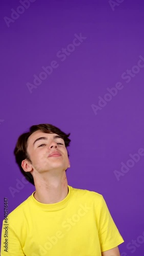Positive teenager boy pointing up to copy space isolated on purple background