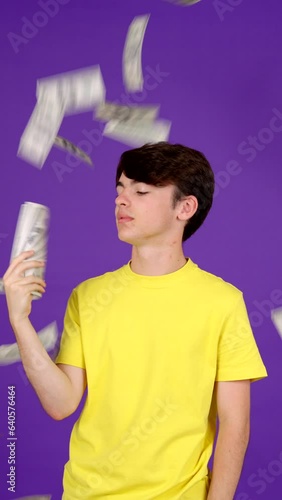 Rich teenager boy surrounded by money. Bills flying on air isolated on purple background