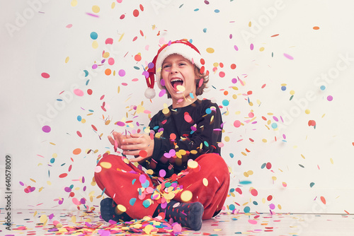 Smiling boy in Santa hat under colorful confetti