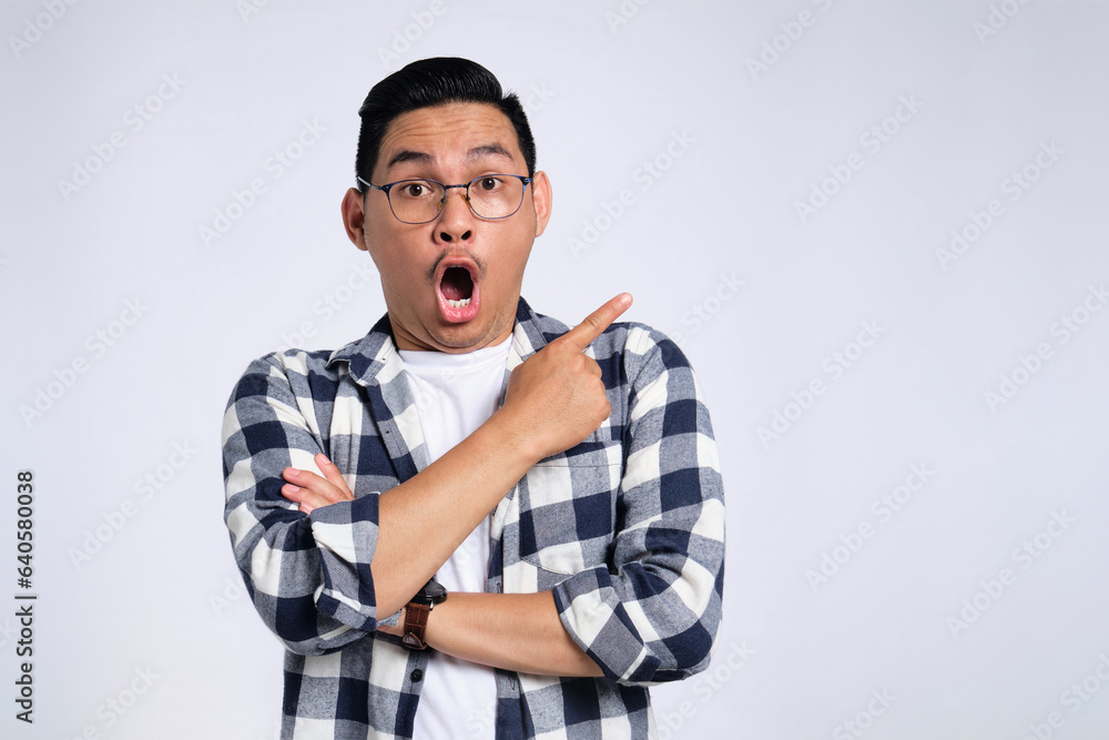Excited young Asian man in casual shirt pointing finger at copy space, presenting sale offer isolated on white background Excited young Asian man in casual shirt pointing finger at copy space, presenting sale offer isolated on white background