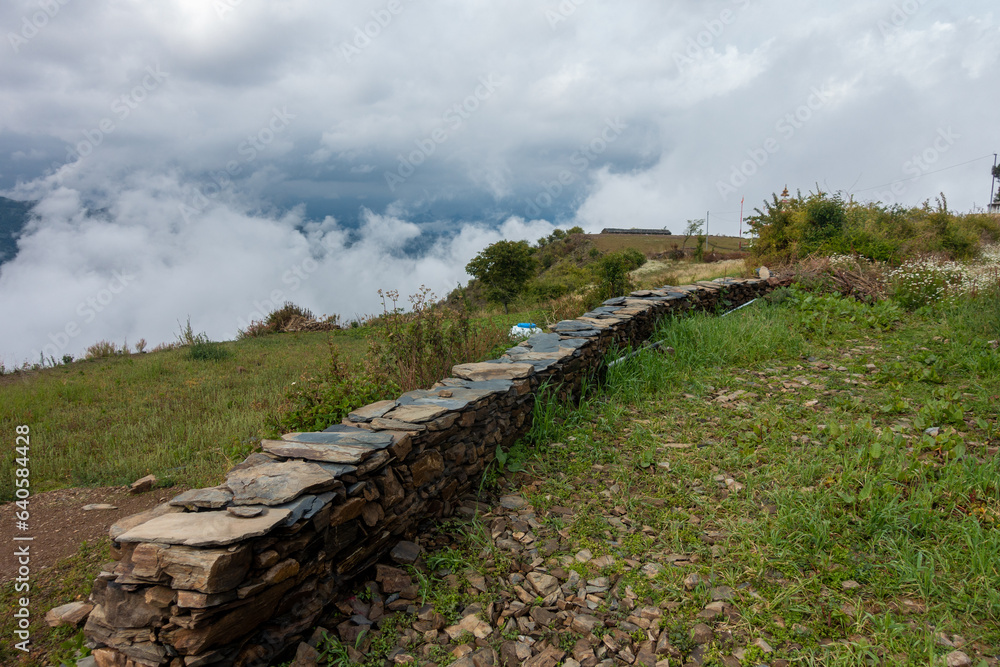 Rural stone wall amidst Himalayan mountains, Uttarakhand, India. Scenic countryside view.