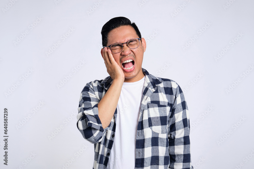Dental problems. Unhappy young Asian man in casual shirt suffering from severe toothache, touching his cheek isolated on white background Dental problems. Unhappy young Asian man in casual shirt suffering from severe toothache, touching his cheek isolated on white background