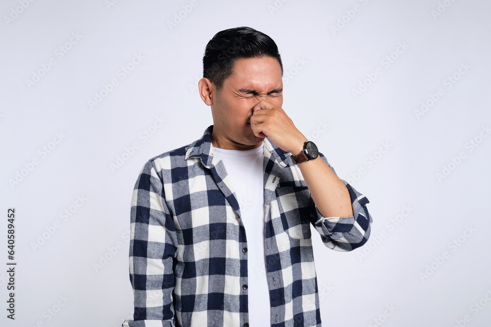 Young Asian man in casual shirt holding breath with finger on nose, smelling something stinky and disgusting isolated on white background Young Asian man in casual shirt holding breath with finger on nose, smelling something stinky and disgusting isolated on white background