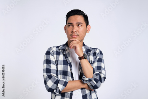 Making Decision. Pensive young Asian man in casual shirt looking up, touching his chin, thinking about question isolated on white background