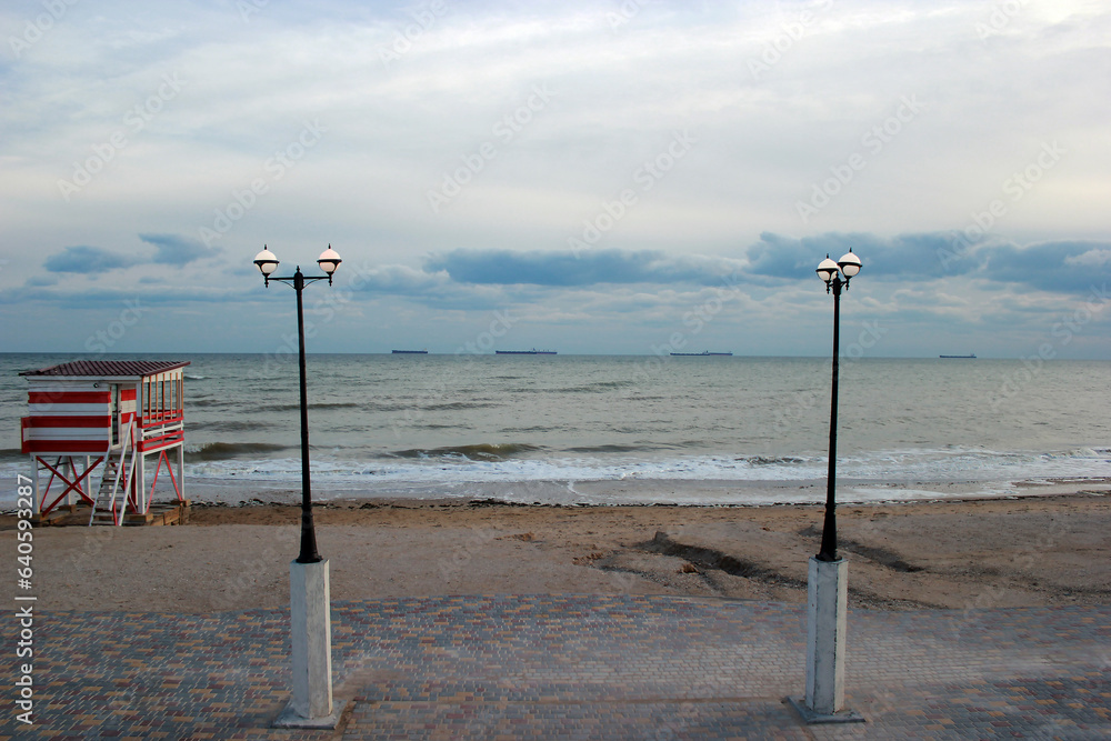 Two lanterns stand on the sea coast against the background of clouds and the sea horizon