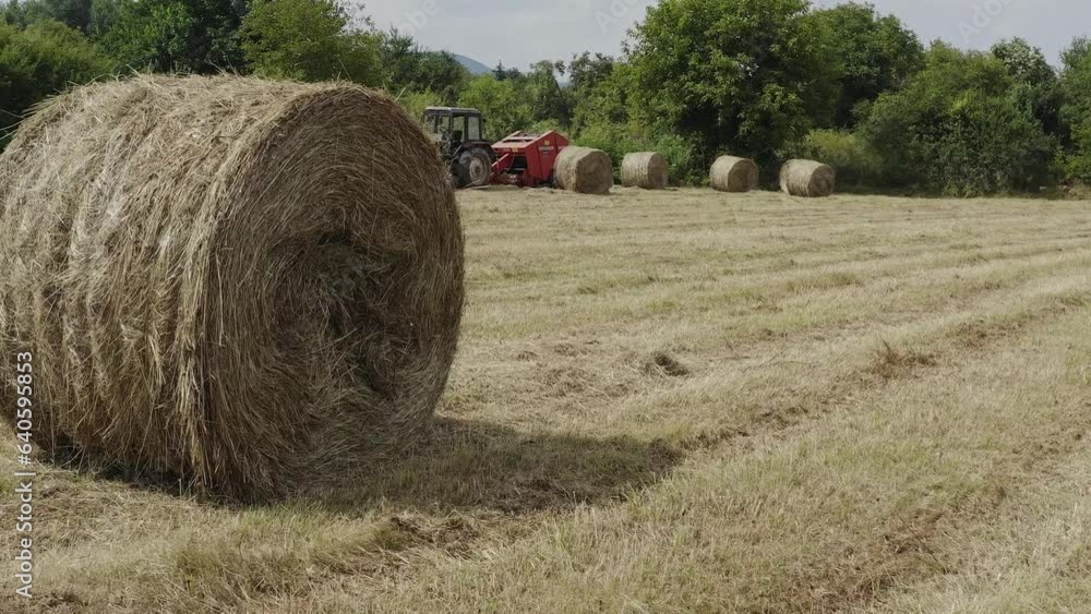 Slide shot reveals farm machinery in field with golden bales of hay Slide shot reveals farm machinery in field with golden bales of hay