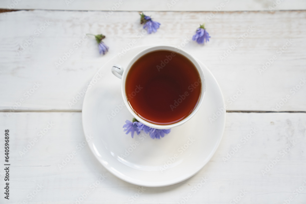 Top view, flat surface. Drink from chicory roots in a cup, a flowering chicory plant on a white wooden table. An alternative to decaffeinated coffee. High quality photo